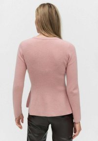 Pull en tricot rose à manches longues, au design ajusté et à l'ourlet légèrement évasé. Le matériau semble doux et texturé.
