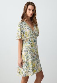 Abito con stampa floreale caratterizzato da scollatura a V, maniche corte e forma ad A. I colori includono verde, giallo e morbidi accenti pastello.