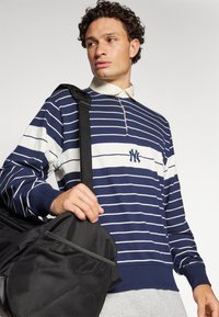 Navy and white striped long-sleeve pullover with a collar and NY logo, paired with a black bag featuring a mesh pocket.