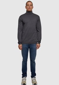 Graham turtleneck-Pullover mit langen Ärmeln, kombiniert mit blauen Jeans und mehrfarbigen Sportschuhen. Einfaches und figurbetontes Design.
