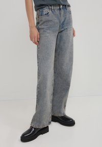 Jeans ampi e chiari in denim, caratterizzati da una vita alta, cuciture in evidenza e una vestibilità rilassata. Abbinati a scarpe con platform nere.