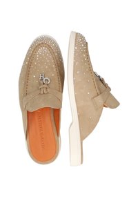 Beige suède instap schoenen met platte witte zolen, versierd met heldere studs en een zilveren logo accent op de bovenkant. De binnenkant heeft een oranje voering.