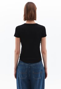 Sort tætsiddende t-shirt med korte ærmer, parret med højtaljede blå denimbukser med to baglommer og synlige syninger.
