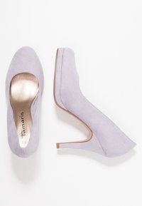 Ljus lavendel pumps med en mjuk mocka-textur, rund tå och en guldfärgad metallinlägg. Klacken är smal och avsmalnande.