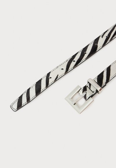 Ceinture en cuir noir et blanc à rayures zébrées, avec plusieurs trous de réglage et une boucle rectangulaire argentée sur fond blanc.