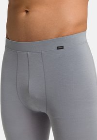 Leggings de algodón gris que presentan una textura suave, cinturilla elástica y una pequeña etiqueta de la marca en la parte delantera cerca de la cinturilla, con un diseño ajustado.