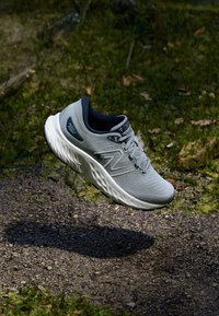 Light gray athletic shoe with a textured upper, featuring a black accent on the heel and a white cushioned sole. Laces visible on top.