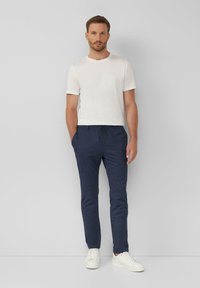 Weißes Baumwoll-T-Shirt und marineblaue Strick-Jogginghosen mit Kordelzug, kombiniert mit weißen Sneakers. Glatte Textur, lässiges Design, slim fit.