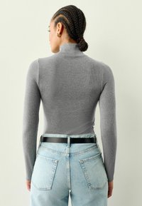 Enganliegendes graues Langarmtop mit einem Mockneck, kombiniert mit hoch taillierten, hellblauen Jeans und einem schwarzen Gürtel. Glatte Textur und gerippter Stoff.