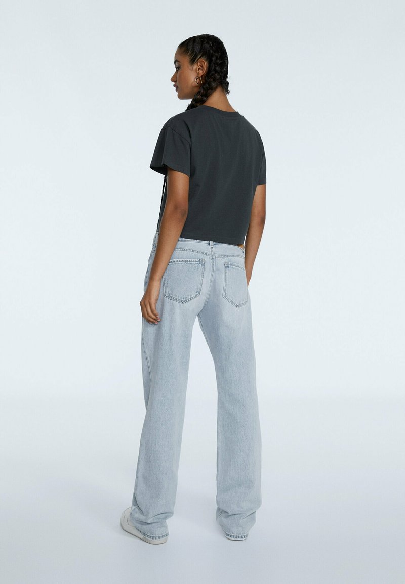 Graues, kurz geschnittenes T-Shirt, kombiniert mit hellblauen weit geschnittenen Jeans. Die Jeans haben ein klassisches Fünf-Taschen-Design und leichte Used-Waschungen.