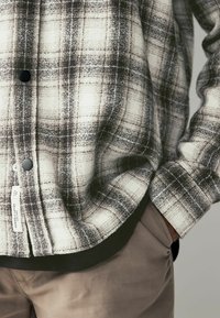 Karierte Hemd in Grau und Weiß, strukturierter Stoff mit Knopfverschluss und schwarzen Akzenten. Verfügt über ein sichtbares Etikett und ein abgerundetes Saumdesign.