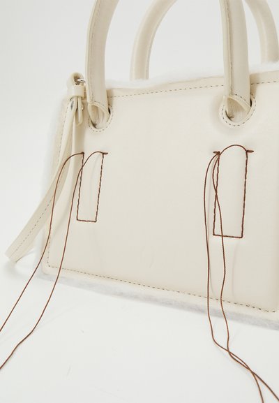 Cream white handbag with a structured design, featuring leather material, short handles, brown stitching, and soft textured accents.