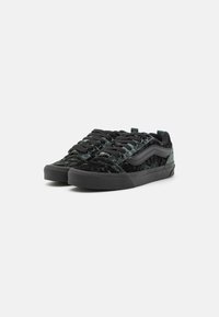 Adidași din catifea neagră cu un finisaj texturat, având șireturi negre și o bandă laterală contrastantă neagră. Talpa din cauciuc pentru tracțiune.