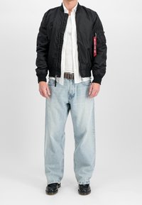 Svart bombarjacka med ribbade mudd och nederkant. Vit knappad skjorta under. Ljusblå baggy jeans. Svarta skor. Röd etikett på jackan.