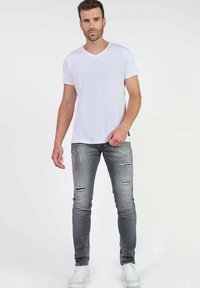 Witte v-hals t-shirt, slimfit grijze ripped jeans en witte sneakers. De outfit heeft een casual, minimalistisch ontwerp en zachte texturen.