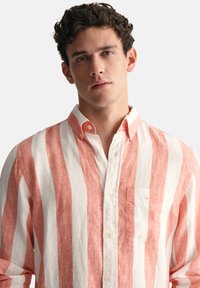 Pruhovaná košile s širokými korálovými a bílými horizontálními pruhy, límečkem na knoflíky, náprsní kapsou a měkkou lněnou texturou.
