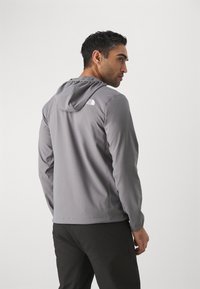 Grijze lichtgewicht jas met een capuchon, voorzien van het "The North Face" logo in het wit op de achterkant, een soepele textuur en een getailleerd design.