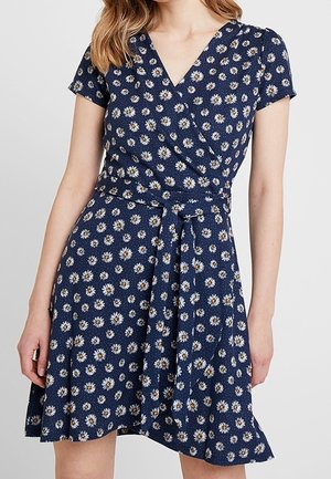 Navy blue wrap dress with short sleeves and white daisy print, tied waist, worn by a woman with loose hair.