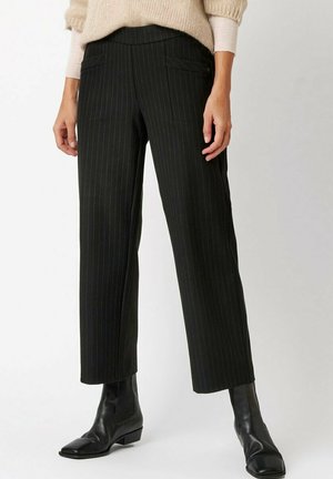 Schwarze Nadelstreifenhose mit maßgeschneiderter Passform, ausgestattet mit Fronttaschen, glatter Textur und verkürzter Länge, kombiniert mit eleganten schwarzen Stiefeletten.