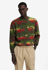 Groen camouflage trui met rode en gele accenten, geribbelde manchetten en zoom, gecombineerd met beige broek met elastische tailleband.