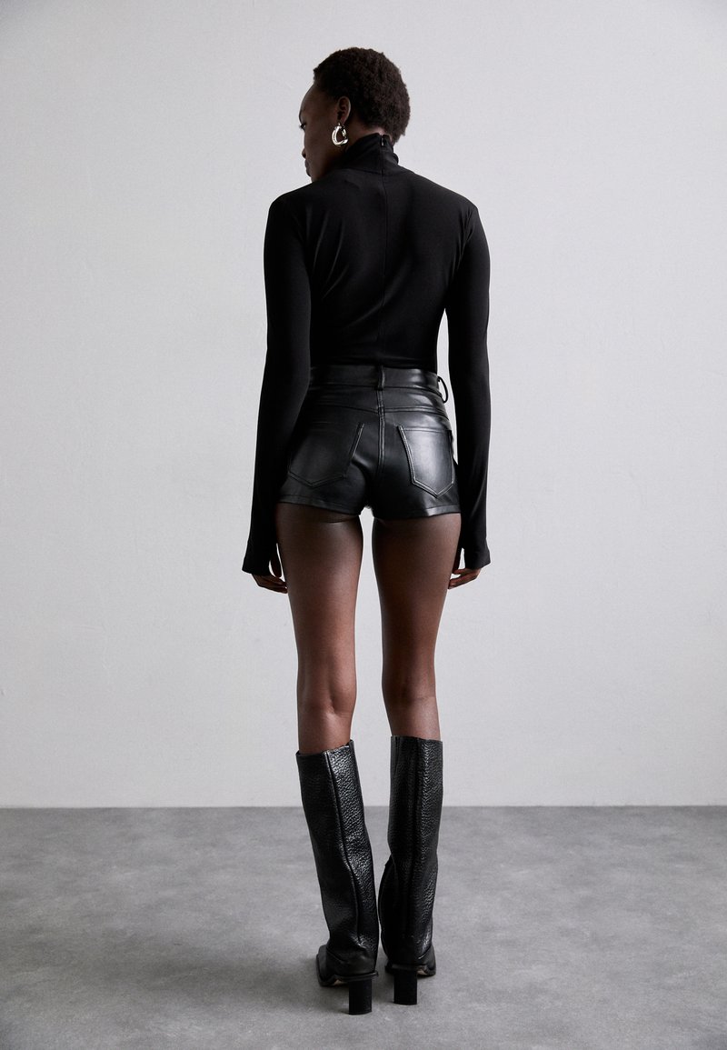 Top negro de manga larga con cuello alto, combinado con shorts de cuero negro de cintura alta. Botas negras hasta la rodilla con tacones apilados.