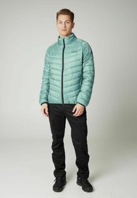 Svijetlosmeđa izolirana jakna s patentnim zatvaračem, koja ima vertikalne šavove i ovratnik, u kombinaciji s crnim hlačama i crnom obućom.