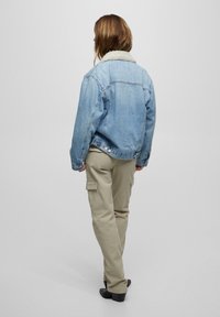 Farkkutakki, jossa on karvainen kaulus, vaaleansininen väri, rento malli, yhdistetty beigenvärisiin cargo-housuihin ja mustiin korollisiin saappaisiin.