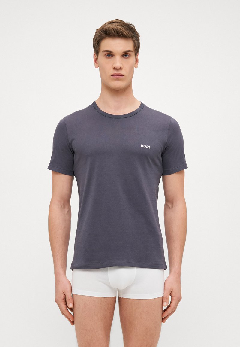 T-shirt navy à manches courtes en tissu doux avec encolure ras du cou et petit logo blanc "BOSS" sur la poitrine gauche. Modèle portant des sous-vêtements blancs.