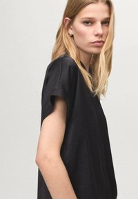 Czarna bluzka z krótkim rękawem o luźnym kroju, gładkiej fakturze i prostym designie. Posiada okrągły dekolt i minimalne zdobienia.