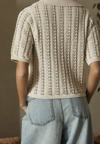 Pull tricoté de couleur crème avec un motif texturé, manches courtes et col côtelé. Assorti à un jean en denim bleu clair, avec des poches arrière.