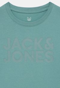 Türkizkék környakú póló elülső részén dombornyomott "JACK & JONES" felirattal, valamint a gallér belsejében kis kutyafej ikon nyomattal.