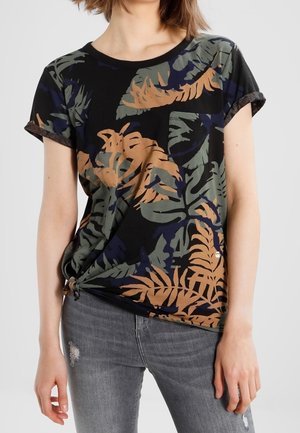 Czarny t-shirt z krótkim rękawem, ozdobiony zielono-brązowym wzorem liści, z podwiniętymi rękawami i wiązaniem na dole. Noszony z szarymi dżinsami.