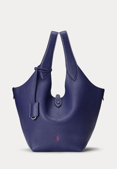 Mørkeblå textured læder tote taske med rundede håndtag og lille rødt logo nær bunden, vist mod en ensfarvet baggrund.
