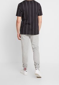 Zwarte T-shirt met witte verticale strepen, gecombineerd met grijze sweatpants. Witte sneakers maken de outfit compleet en tonen een casual ontwerp.