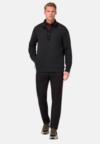 Čierny pulóver s polozipsovým golierom a textúrovanou látkou, skombinovaný s čiernymi nohavicami a hnedými teniskami s svetlými akcentmi.
