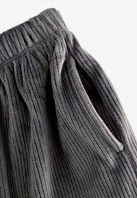Pantaloni in tessuto a costine grigi con superficie testurizzata, dotati di una vita elastica e tasca laterale. Materiale morbido con strisce scure variegate.