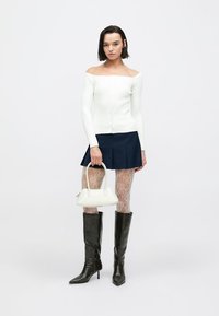 Bela bluza z odkritimi rameni, mornarsko modra nabrana krilo, mrežaste nogavice, črni škornji do kolen in majhna bela torbica. Teksturirani in oprijeti materiali.