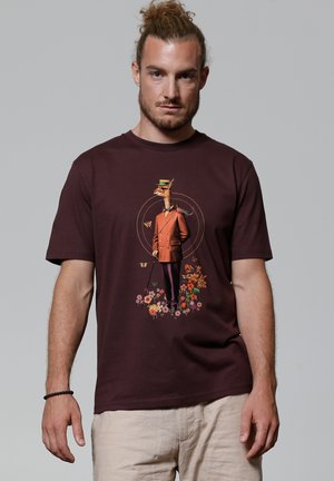 Bordeaux T-shirt met een speelse afbeelding van een giraffe in een bruine pak met bloemaccenten aan de onderkant. Korte mouwen, ronde hals.