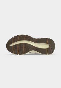 Semelle de chaussure avec bande de roulement brun foncé et insert de soutien de la voûte plantaire beige, présentant des motifs de grip texturés et le nom de la marque embossé près du talon.