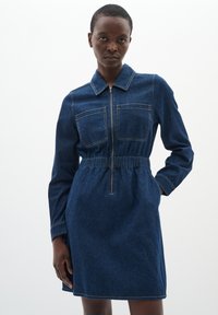 Jeans jurk met een rits aan de voorkant, kraag, lange mouwen en elastische taille. Diepblauwe kleur met twee borstzakken en contrasterende stiksels.