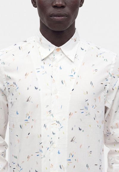 Homme portant une chemise blanche à boutons, col pointu et petits gribouillis abstraits multicolores.