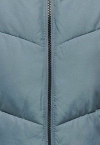 Padded blue jacket with a zigzag quilted pattern, featuring a central black zipper and smooth, matte fabric texture.