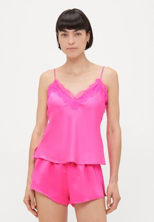 Camisola di raso rosa con bordi in pizzo e spalline regolabili, abbinata a pantaloni corti coordinati con vestibilità rilassata e spacchi laterali.