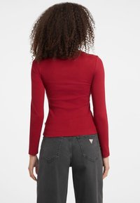 Top a maniche lunghe rosso a coste con design aderente, abbinato a jeans grigi scuri a vita alta con tasche posteriori e etichetta del logo.