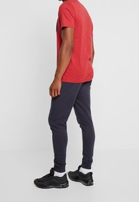 Röd prickig t-shirt med korta ärmar, kombinerad med marinblå joggers. Svarta sneakers med synlig luftkuddning har en elegant design.