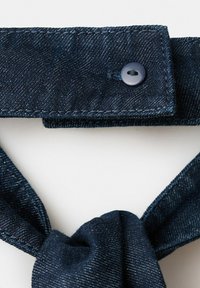 Cravate en denim bleu foncé avec une patte boutonnée et un nœud noué sur un fond clair.
