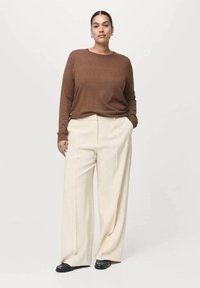 Brun langærmet top sat sammen med creme farvede brede bukser. Sorte sko fuldender outfittet. Glat stof med minimal detaljering.
