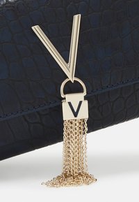 Bolso de cuero texturizado en color navy con un acento de herrajes en forma de V en tono dorado y borlas de cadena dorada en cascada.