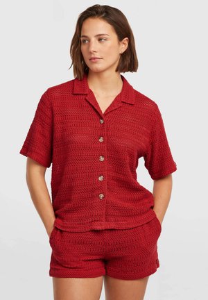 Rød strikket kortærmet skjorte med krave, fem knapper og matchende shorts. Tekstureret mønster med åbent væv og sidelommer.