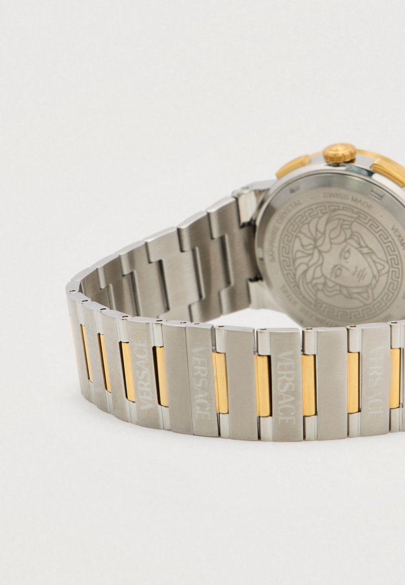 Edelstahluhr mit goldfarbenen Akzenten, die eine Mischung aus glänzenden und gebürsteten Gliedern aufweist, mit "VERSACE" graviert und einem strukturierten Gehäuseboden.